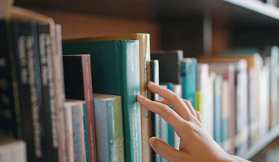 Close up hand search for book on bookshelves in the library. Select a book on shelf. Studying knowledge education in bookstore