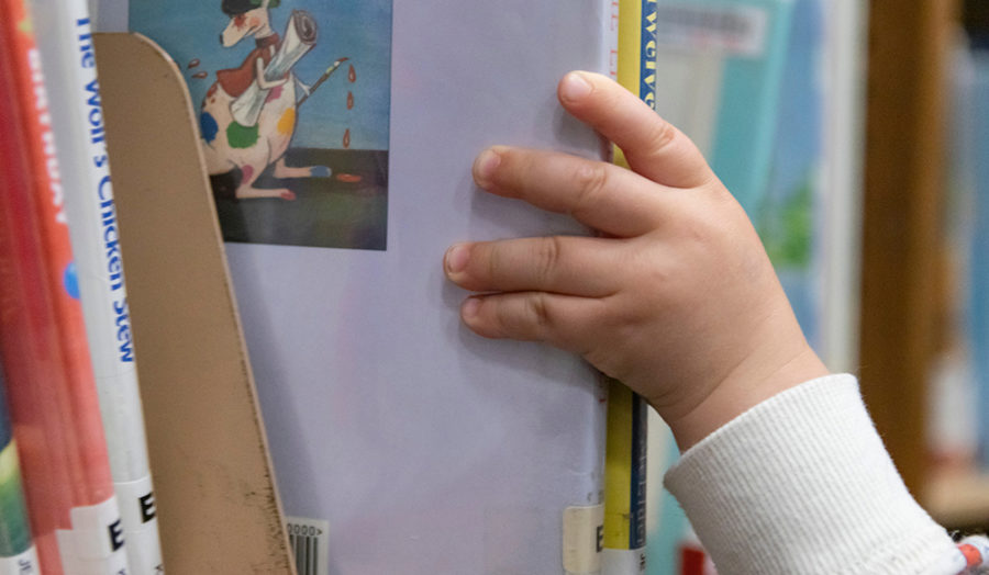 East Brunswick, NJ May 5, 2019 - Child's hand pulling a children's book from a library bookshelf.